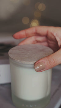 Video showing a ZENTS candle on a book. Hand removes lid and lights wick. Cut to 2 candles burning as a figure in the background reads.